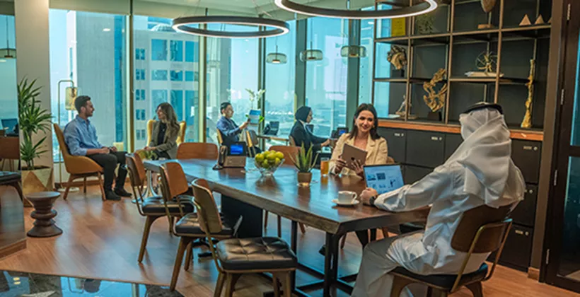 A dynamic shared workspace at Sahab Tower, Kuwait, where professionals collaborate and work individually in a bright, modern setting with large windows offering city views.