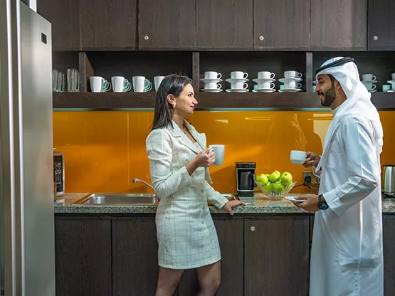 Two professionals having a coffee chat in the modern kitchen area at Sahab Tower, Kuwait, featuring sleek cabinetry and a fully equipped setup.